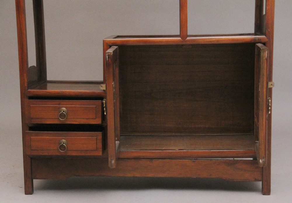 An early 20th-century Chinese hardwood duobaoge cabinet featuring asymmetrical open shelving, geometric side cut-outs, and lower drawers with brass hardware. View V