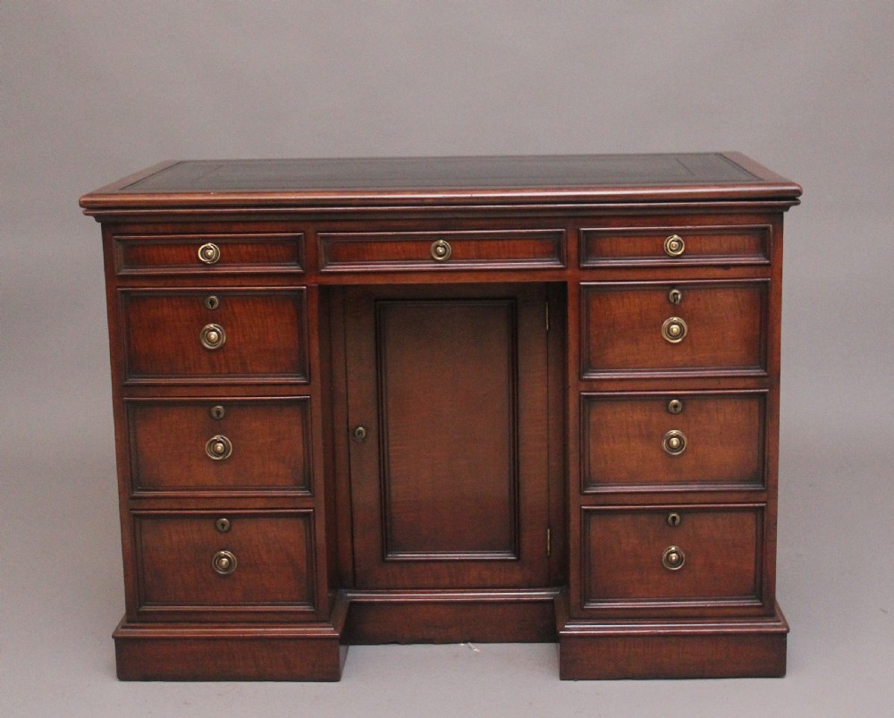 An early 19th-century mahogany kneehole desk with a dark leather writing top, multiple side drawers with circular brass ring handles, and a central recessed cupboard door.