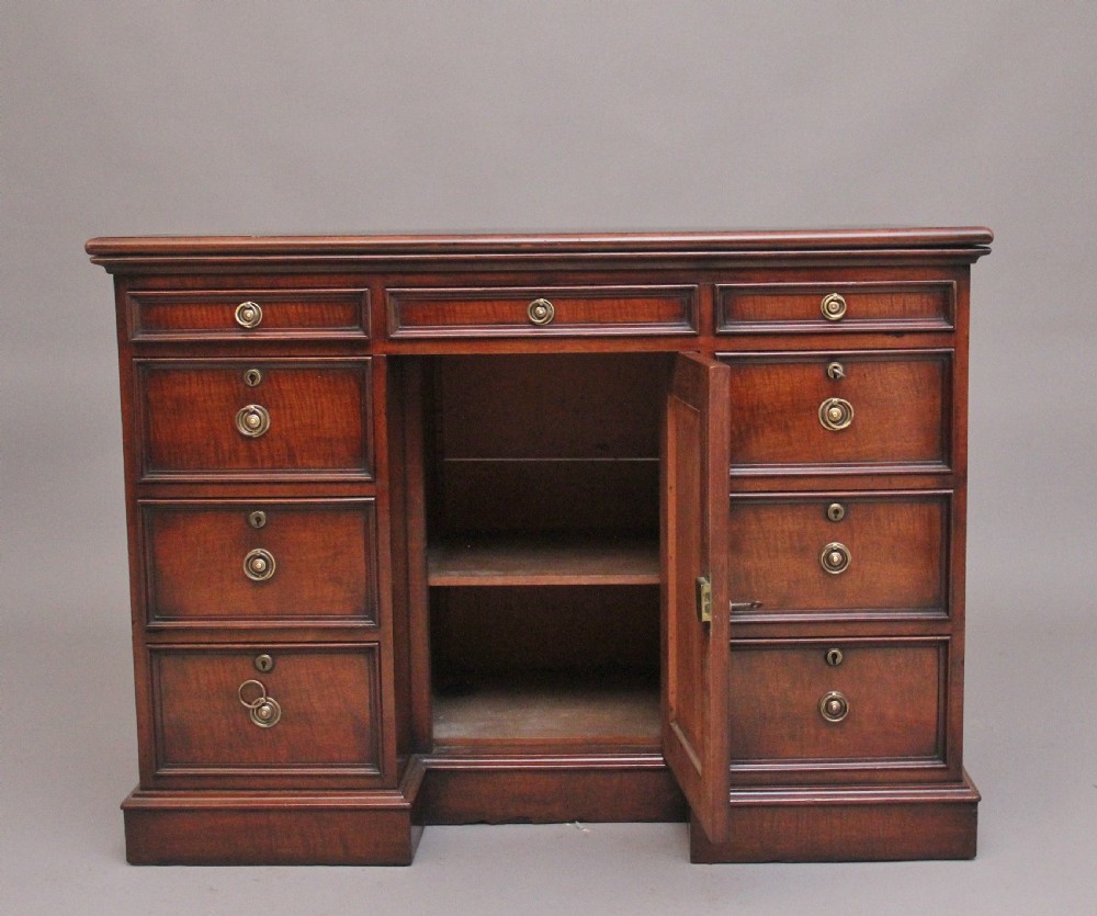 An early 19th-century mahogany kneehole desk with a dark leather writing top, multiple side drawers with circular brass ring handles, and a central recessed cupboard door. View II