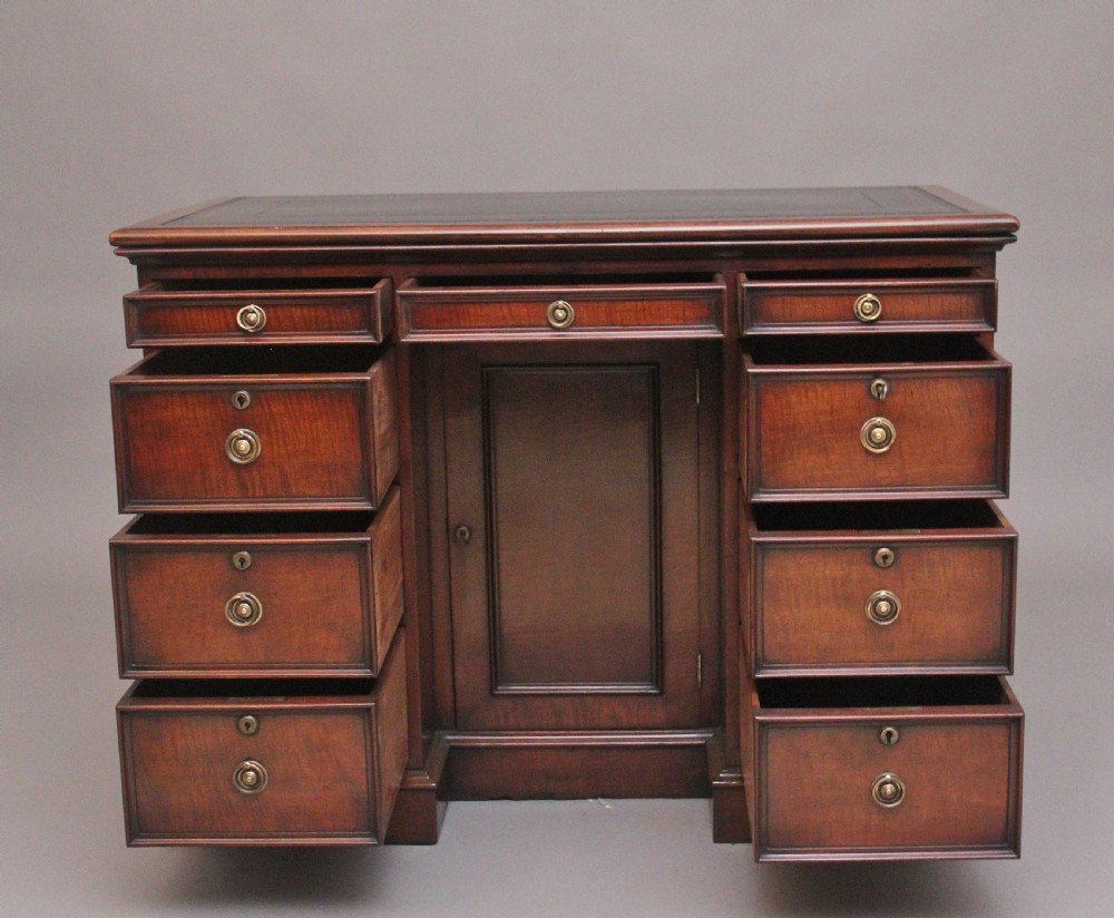 An early 19th-century mahogany kneehole desk with a dark leather writing top, multiple side drawers with circular brass ring handles, and a central recessed cupboard door. View III