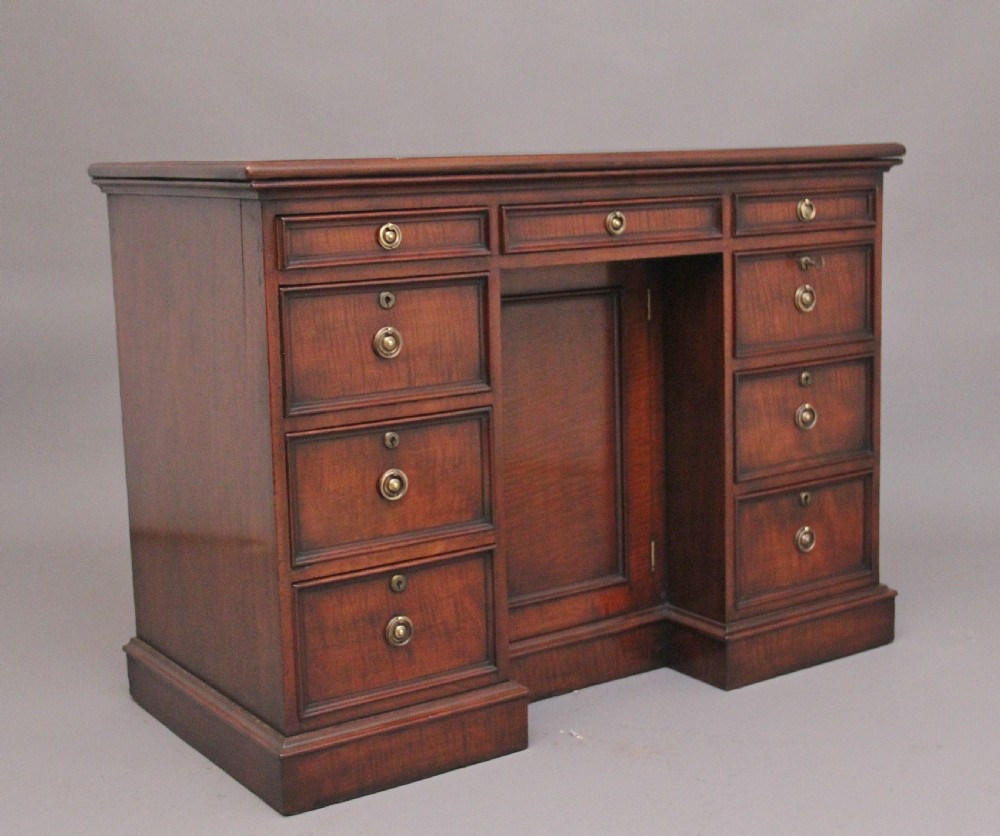 An early 19th-century mahogany kneehole desk with a dark leather writing top, multiple side drawers with circular brass ring handles, and a central recessed cupboard door. View V