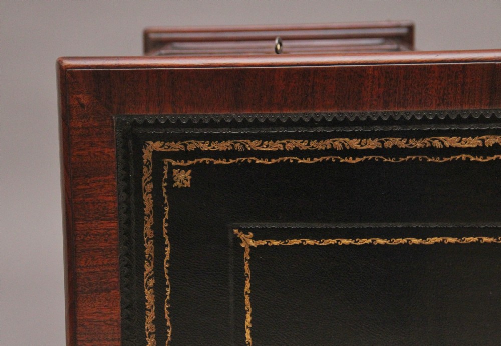An early 19th-century mahogany kneehole desk with a dark leather writing top, multiple side drawers with circular brass ring handles, and a central recessed cupboard door. View X