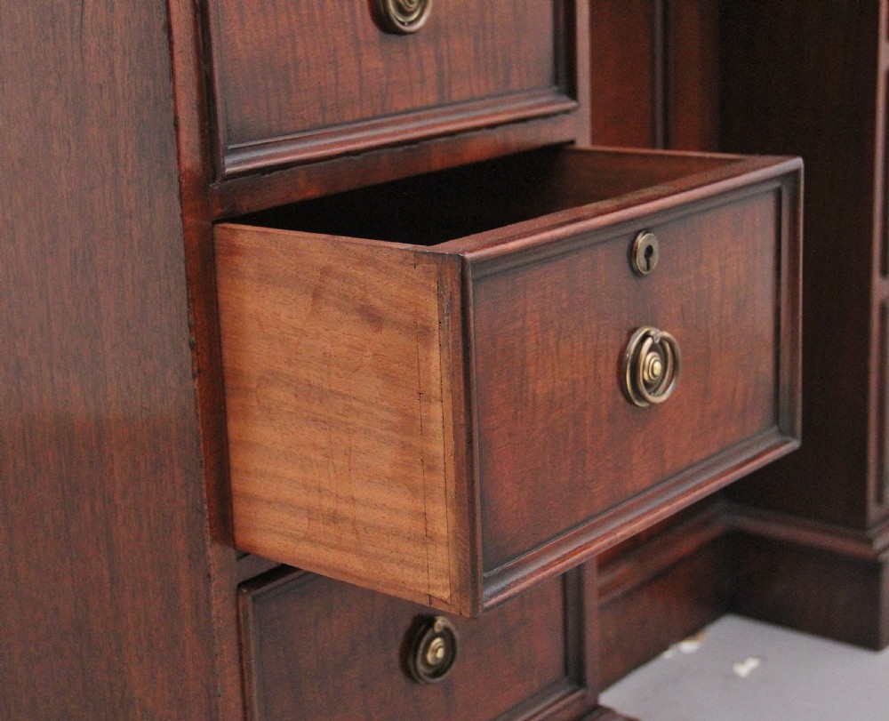 An early 19th-century mahogany kneehole desk with a dark leather writing top, multiple side drawers with circular brass ring handles, and a central recessed cupboard door. View XII