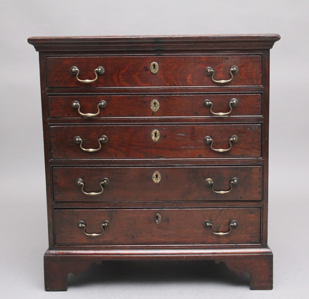 An 18th-century Georgian dark oak chest of drawers featuring five horizontal graduated drawers with brass swan-neck handles, brass escutcheons, and bracket feet.