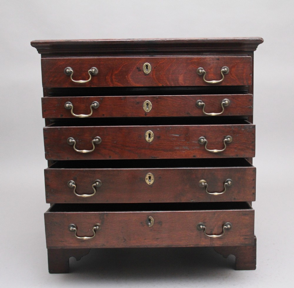 An 18th-century Georgian dark oak chest of drawers featuring five horizontal graduated drawers with brass swan-neck handles, brass escutcheons, and bracket feet. View II