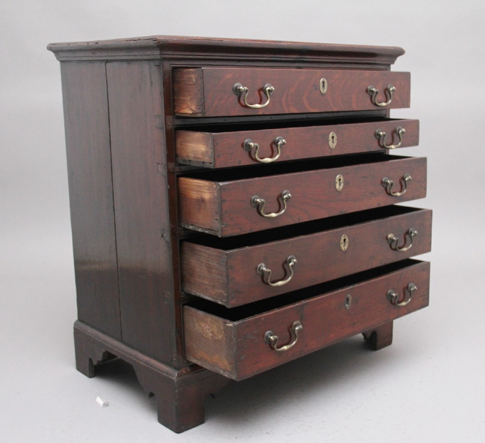 An 18th-century Georgian dark oak chest of drawers featuring five horizontal graduated drawers with brass swan-neck handles, brass escutcheons, and bracket feet. View V