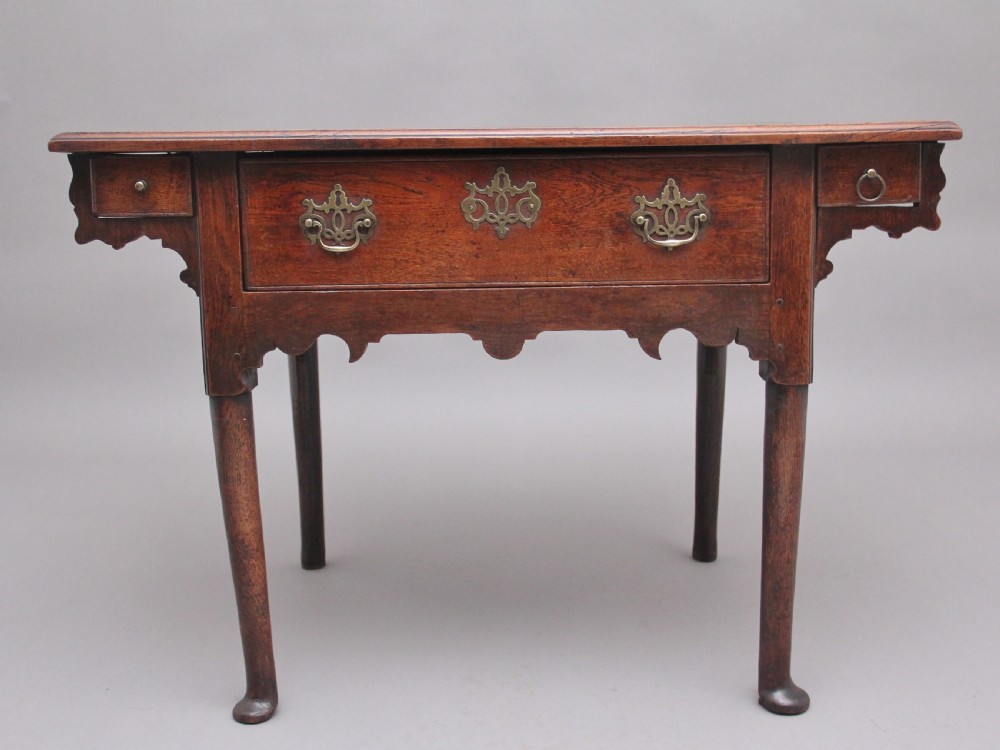 An 18th-century dark oak side table featuring a central drawer, small side drawers, pierced brass handles, a shaped apron, and turned legs ending in pad feet.