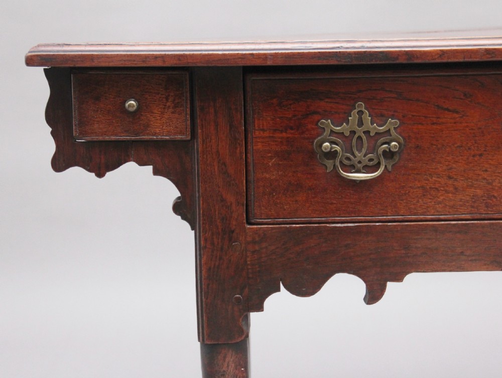 An 18th-century dark oak side table featuring a central drawer, small side drawers, pierced brass handles, a shaped apron, and turned legs ending in pad feet. View II