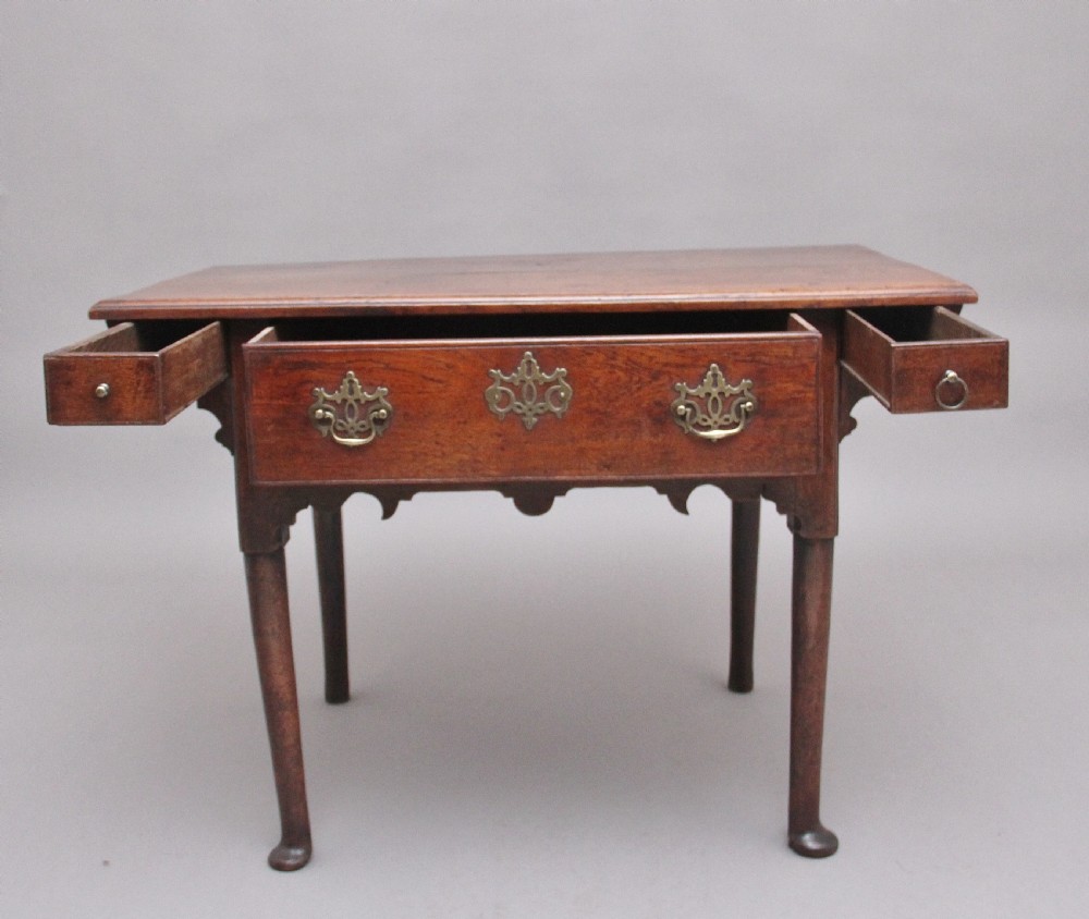 An 18th-century dark oak side table featuring a central drawer, small side drawers, pierced brass handles, a shaped apron, and turned legs ending in pad feet. View III