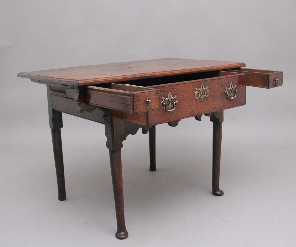 An 18th-century dark oak side table featuring a central drawer, small side drawers, pierced brass handles, a shaped apron, and turned legs ending in pad feet. View VI