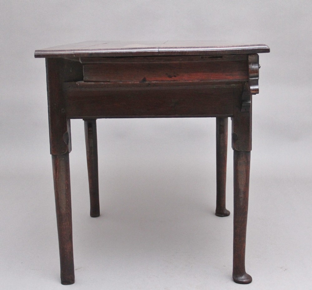 An 18th-century dark oak side table featuring a central drawer, small side drawers, pierced brass handles, a shaped apron, and turned legs ending in pad feet. View VII