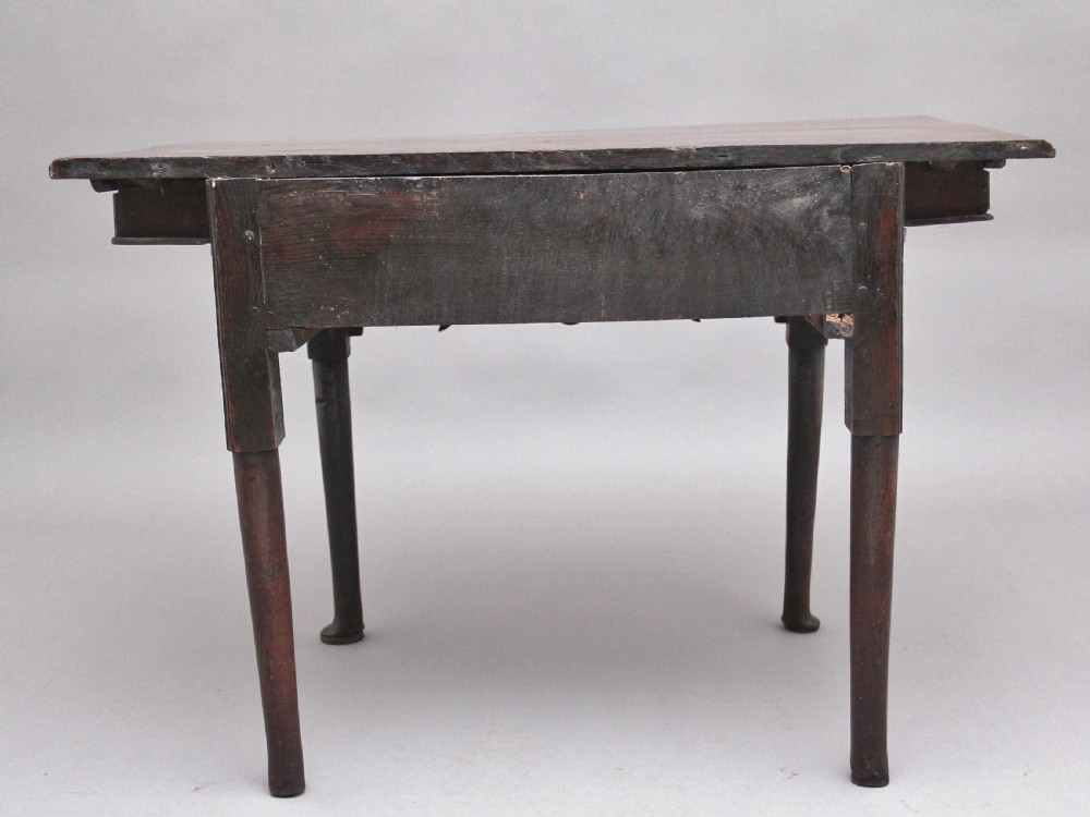 An 18th-century dark oak side table featuring a central drawer, small side drawers, pierced brass handles, a shaped apron, and turned legs ending in pad feet. View VIII