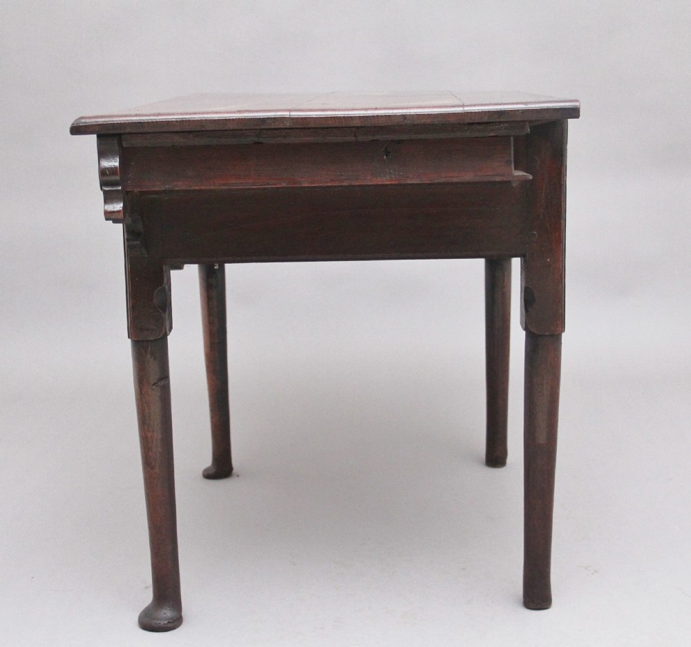 An 18th-century dark oak side table featuring a central drawer, small side drawers, pierced brass handles, a shaped apron, and turned legs ending in pad feet. View IX