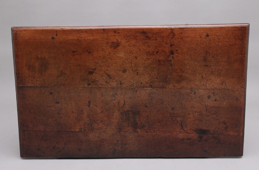 An 18th-century dark oak side table featuring a central drawer, small side drawers, pierced brass handles, a shaped apron, and turned legs ending in pad feet. View X
