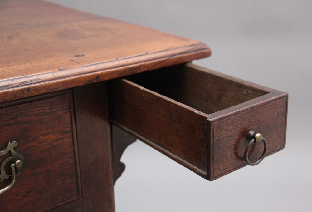 An 18th-century dark oak side table featuring a central drawer, small side drawers, pierced brass handles, a shaped apron, and turned legs ending in pad feet. View XII