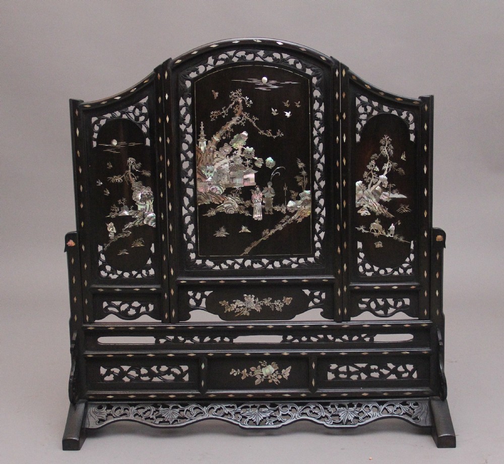 A 19th-century Chinese dark hardwood triptych table screen set with carved openwork borders and detailed mother-of-pearl landscape inlays.
