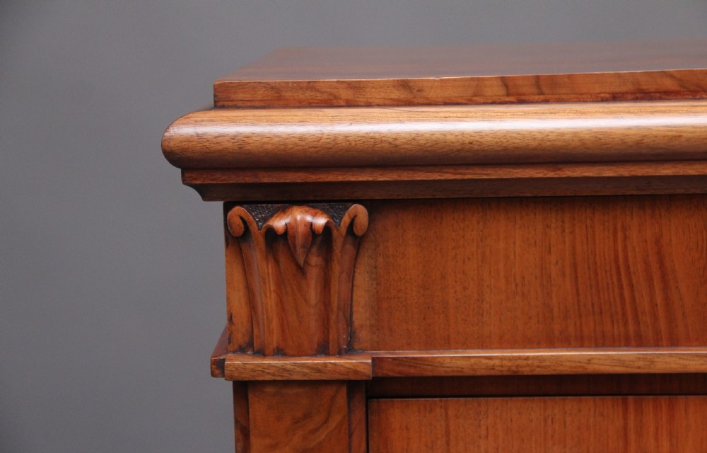 An early nineteenth-century Regency walnut Wellington chest featuring seven drawers with wooden knob handles and carved corbels at the top corners. View VI