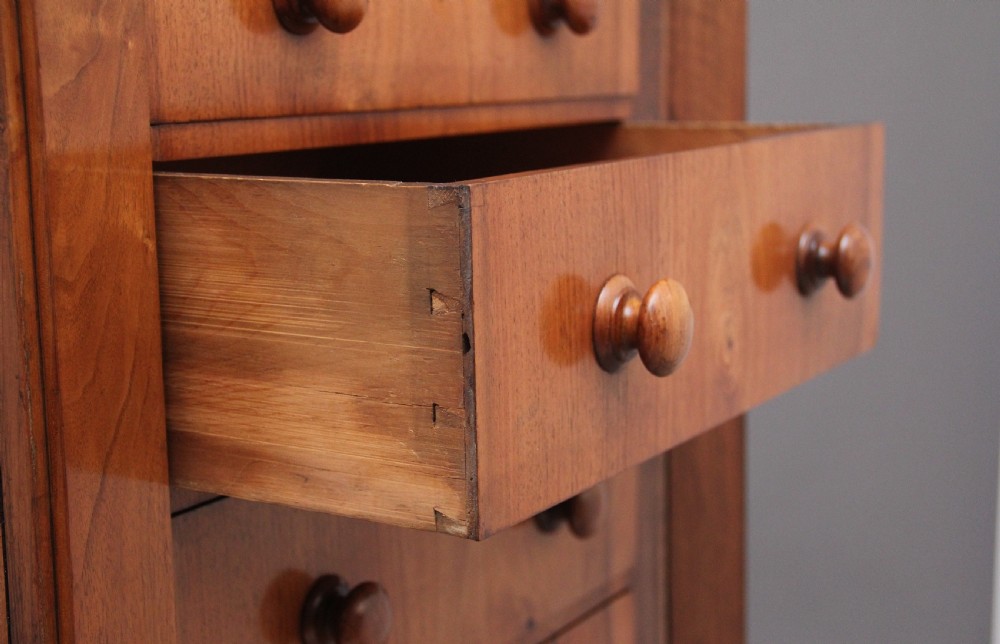 An early nineteenth-century Regency walnut Wellington chest featuring seven drawers with wooden knob handles and carved corbels at the top corners. View VII