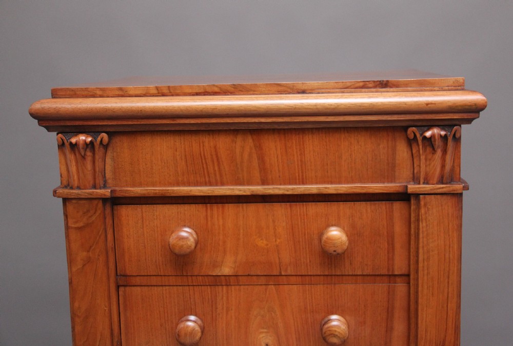 An early nineteenth-century Regency walnut Wellington chest featuring seven drawers with wooden knob handles and carved corbels at the top corners. View VIII