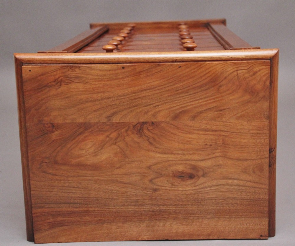An early nineteenth-century Regency walnut Wellington chest featuring seven drawers with wooden knob handles and carved corbels at the top corners. View XIV