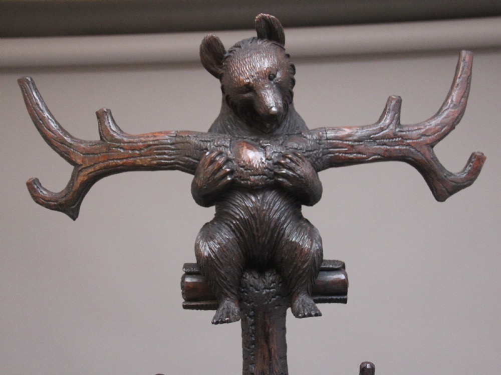 An early twentieth-century carved wooden Black Forest hall stand featuring a tree trunk stem with coat pegs, topped by a bear cub and supported at the base by a larger standing bear with an umbrella hoop and drip pan. View VIII