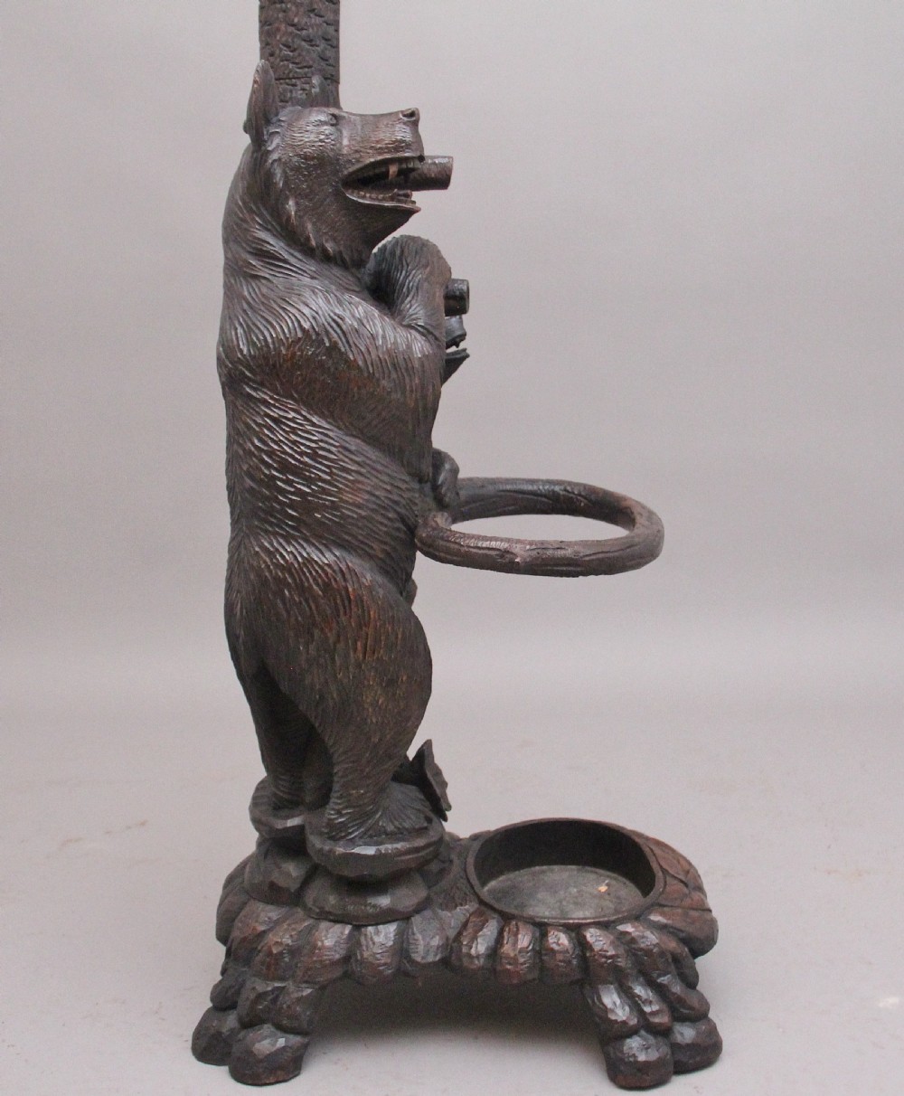 An early twentieth-century carved wooden Black Forest hall stand featuring a tree trunk stem with coat pegs, topped by a bear cub and supported at the base by a larger standing bear with an umbrella hoop and drip pan. View XII