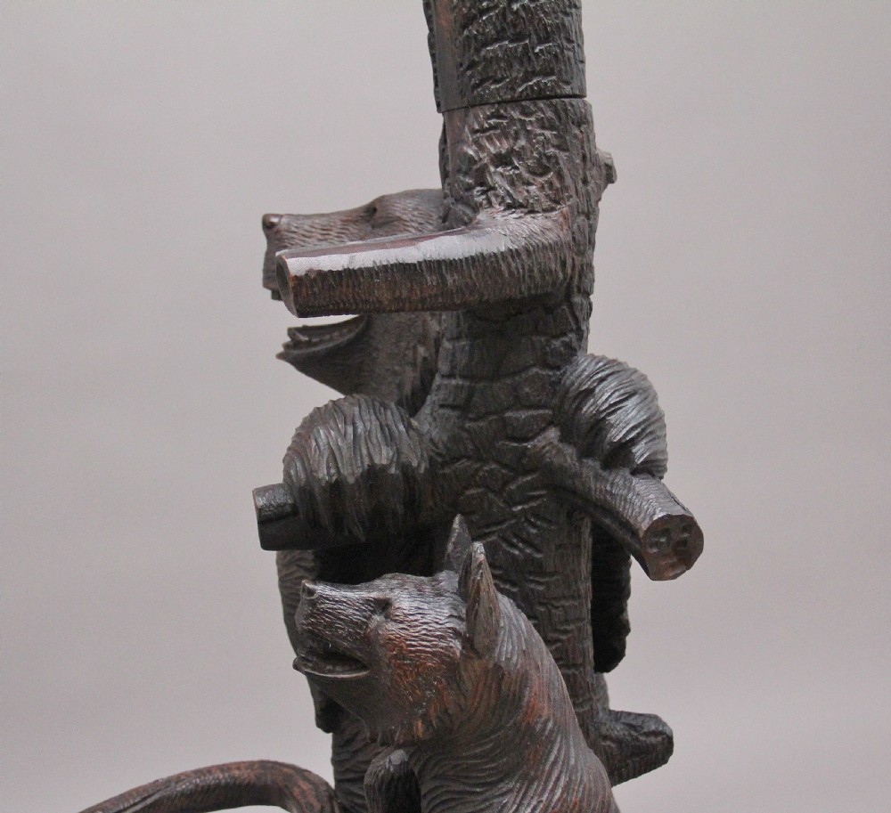 An early twentieth-century carved wooden Black Forest hall stand featuring a tree trunk stem with coat pegs, topped by a bear cub and supported at the base by a larger standing bear with an umbrella hoop and drip pan. View XV
