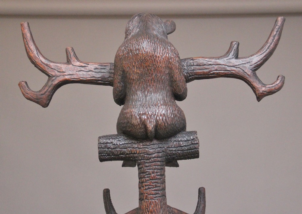 An early twentieth-century carved wooden Black Forest hall stand featuring a tree trunk stem with coat pegs, topped by a bear cub and supported at the base by a larger standing bear with an umbrella hoop and drip pan. View XVI