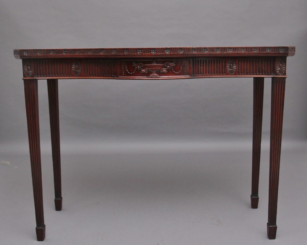 A dark mahogany serpentine console table with fluted legs and carved urn and garland motifs along the apron.