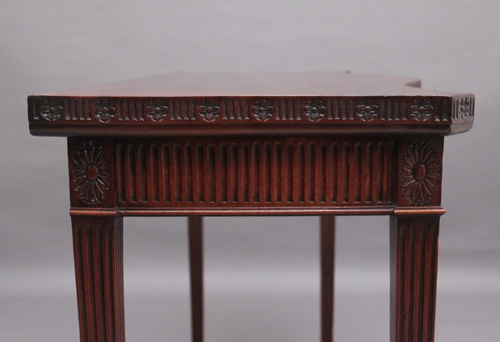 A dark mahogany serpentine console table with fluted legs and carved urn and garland motifs along the apron. View X