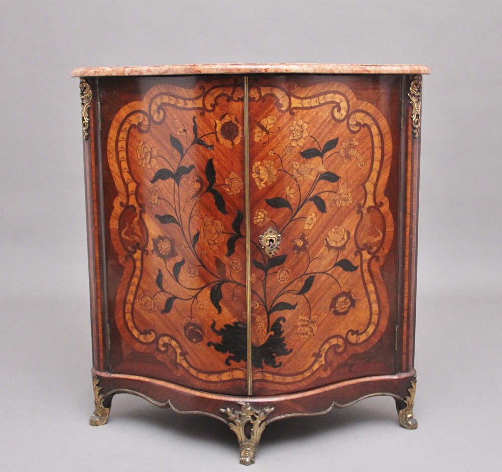 An 18th-century French corner cabinet featuring a curved front with intricate floral marquetry inlay, gilt bronze mounts, and a contoured marble top.