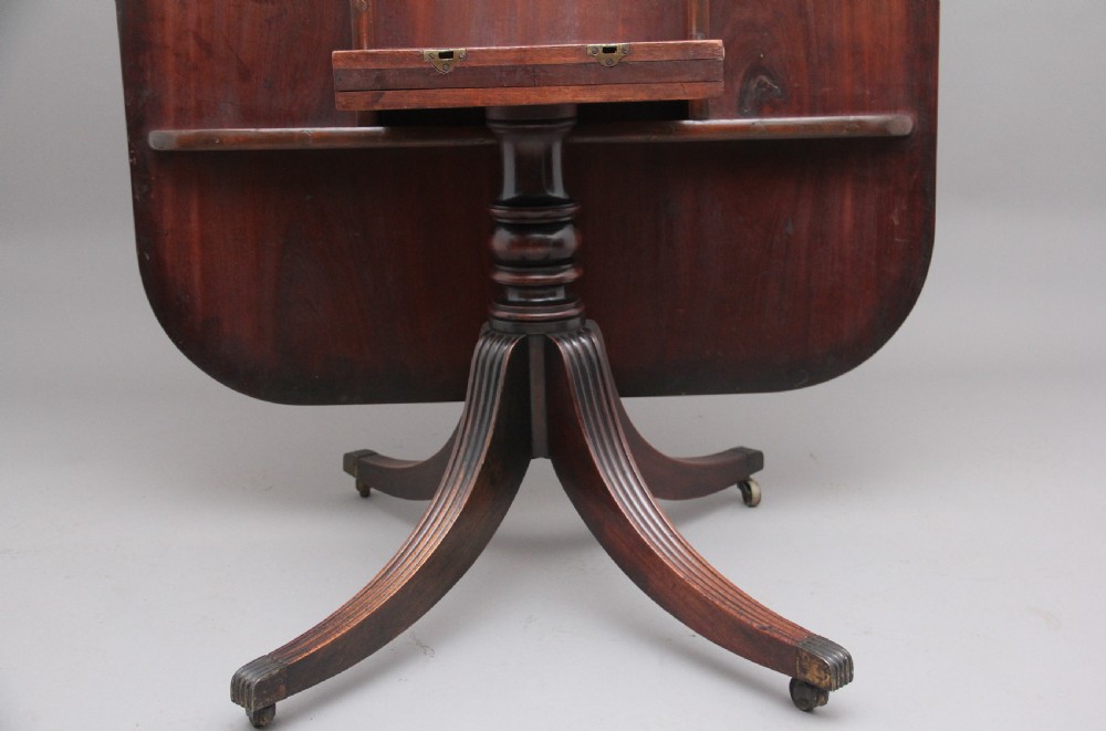 An early 19th-century mahogany tilt-top breakfast table with a rounded rectangular top shown in the upright position above a quadruped pedestal base with brass castors. View VII