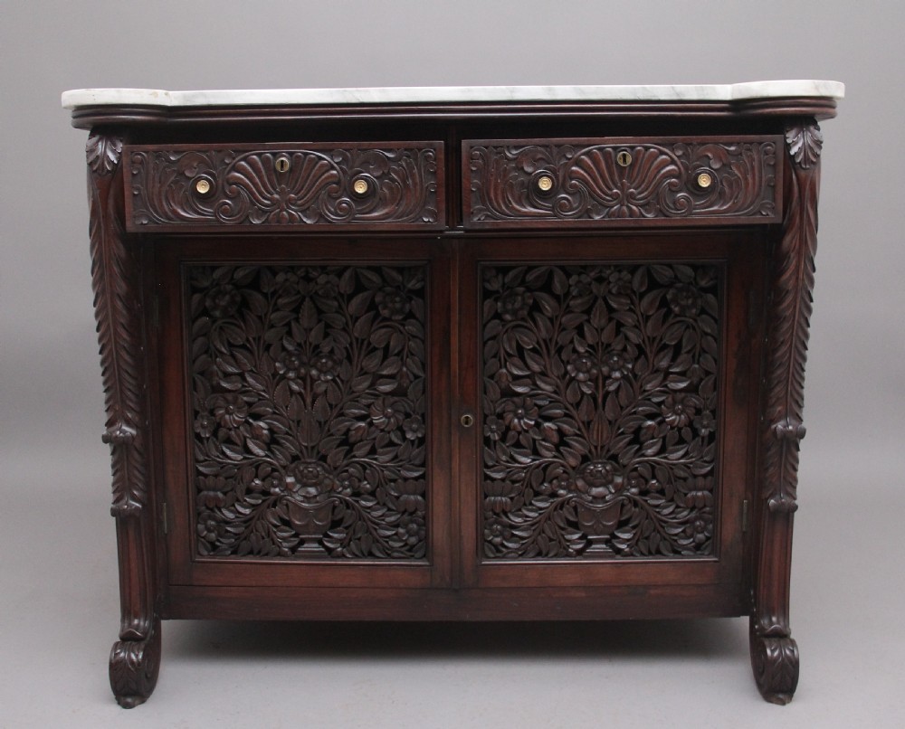 A 19th-century Anglo-Indian dark wood cabinet featuring a white marble top, two carved drawers, and two doors decorated with intricate pierced floral relief motifs. View II