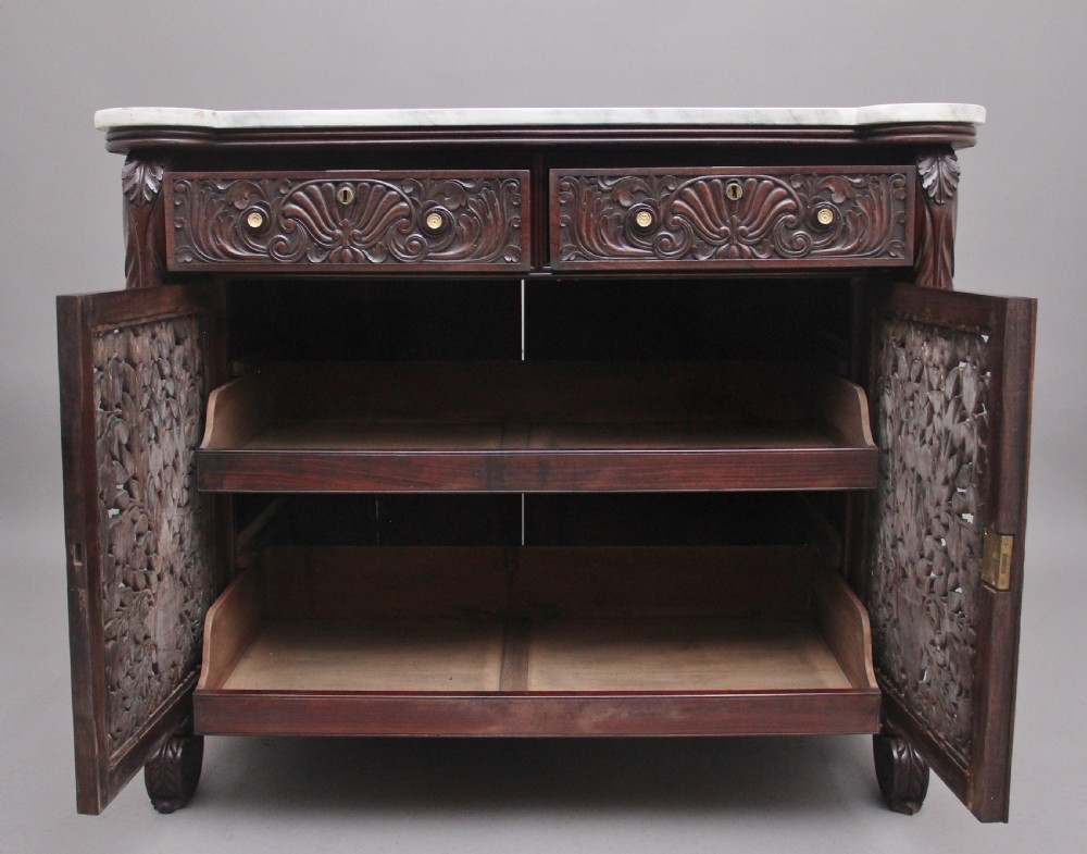A 19th-century Anglo-Indian dark wood cabinet featuring a white marble top, two carved drawers, and two doors decorated with intricate pierced floral relief motifs. View VI