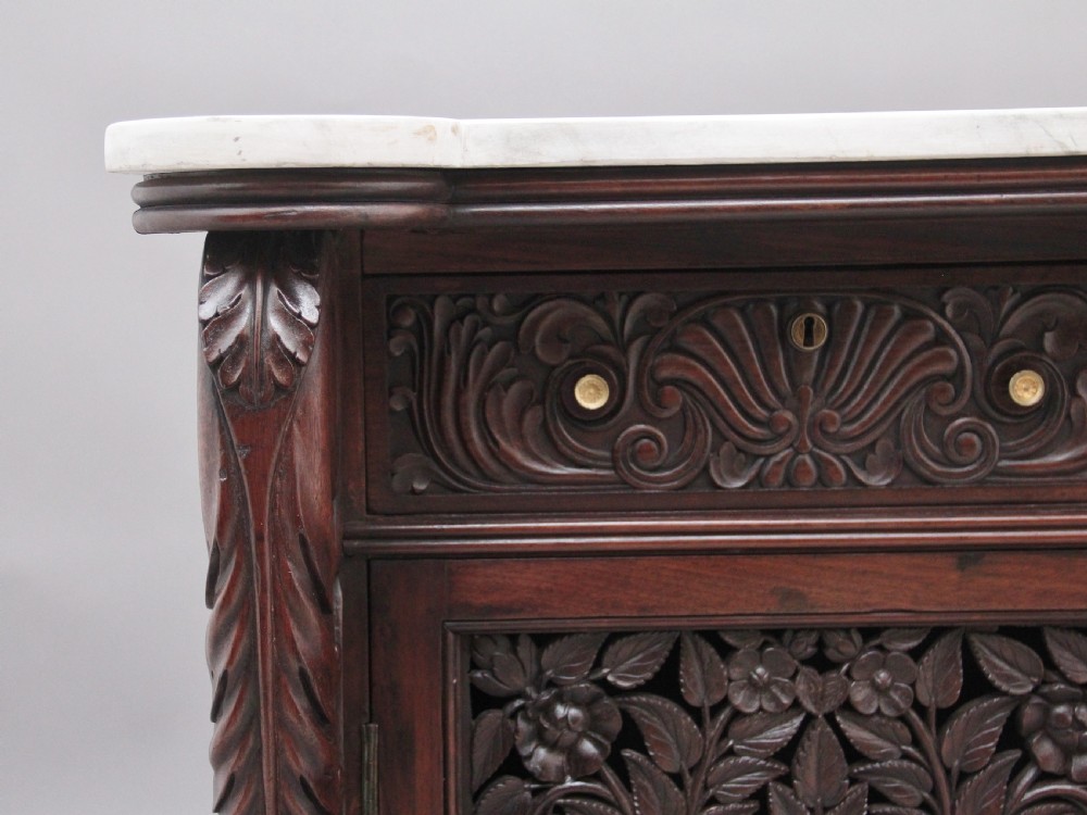 A 19th-century Anglo-Indian dark wood cabinet featuring a white marble top, two carved drawers, and two doors decorated with intricate pierced floral relief motifs. View XII