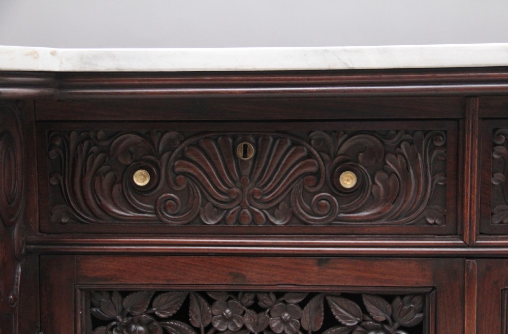 A 19th-century Anglo-Indian dark wood cabinet featuring a white marble top, two carved drawers, and two doors decorated with intricate pierced floral relief motifs. View XIII