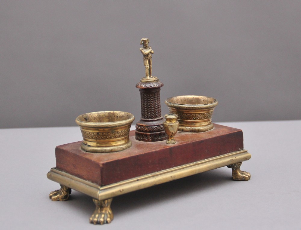 A 19th-century mahogany desk set featuring two metal inkwells, a central column topped with a small gilt figure, and four detailed claw feet.