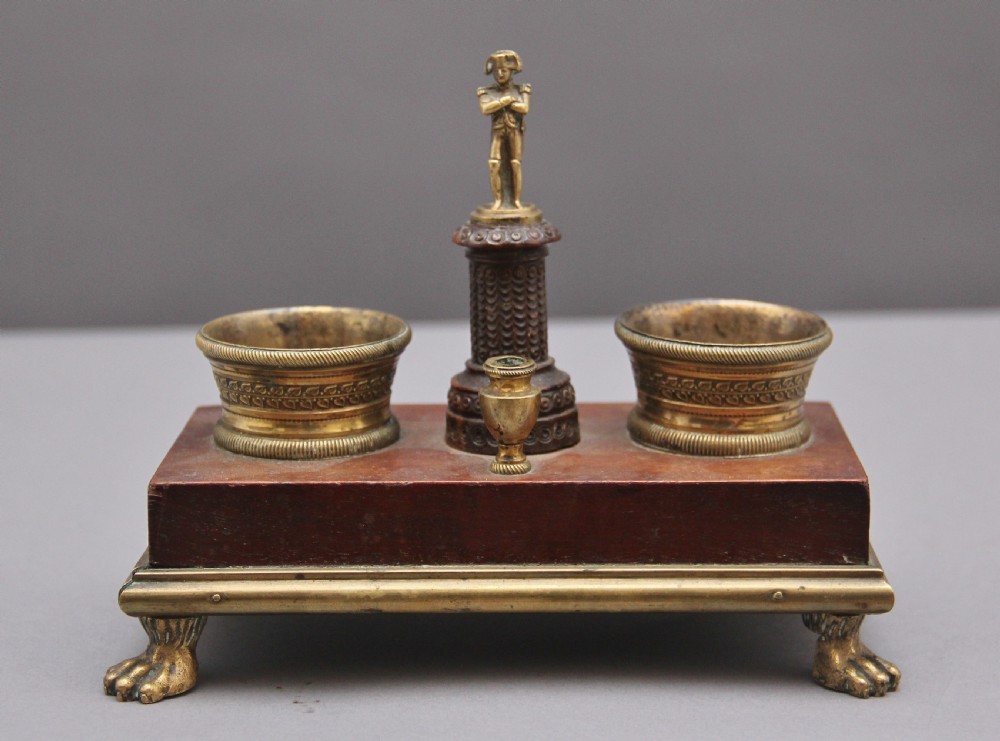 A 19th-century mahogany desk set featuring two metal inkwells, a central column topped with a small gilt figure, and four detailed claw feet. View II