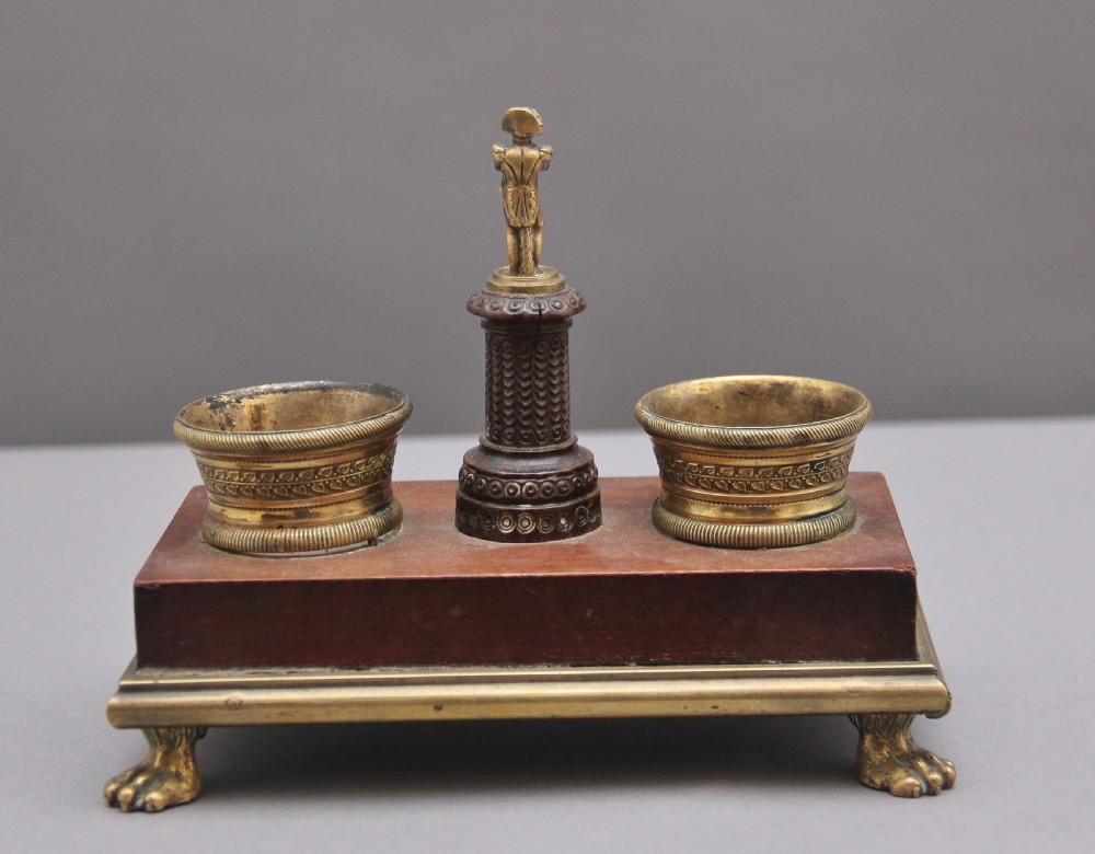 A 19th-century mahogany desk set featuring two metal inkwells, a central column topped with a small gilt figure, and four detailed claw feet. View V