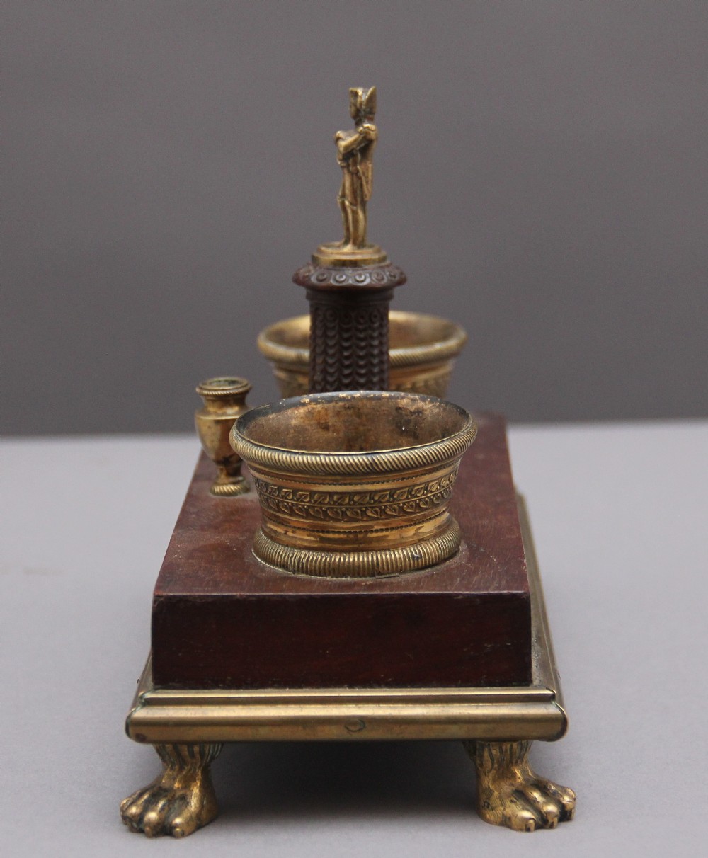 A 19th-century mahogany desk set featuring two metal inkwells, a central column topped with a small gilt figure, and four detailed claw feet. View VII