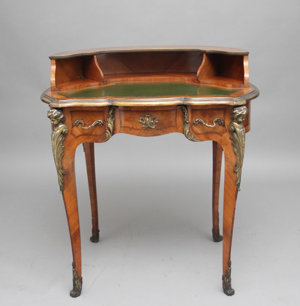 A 19th-century French kingwood writing table featuring ornate gilt-bronze mounts, cabriole legs, a green leather inset top, and a raised shelving superstructure. View V