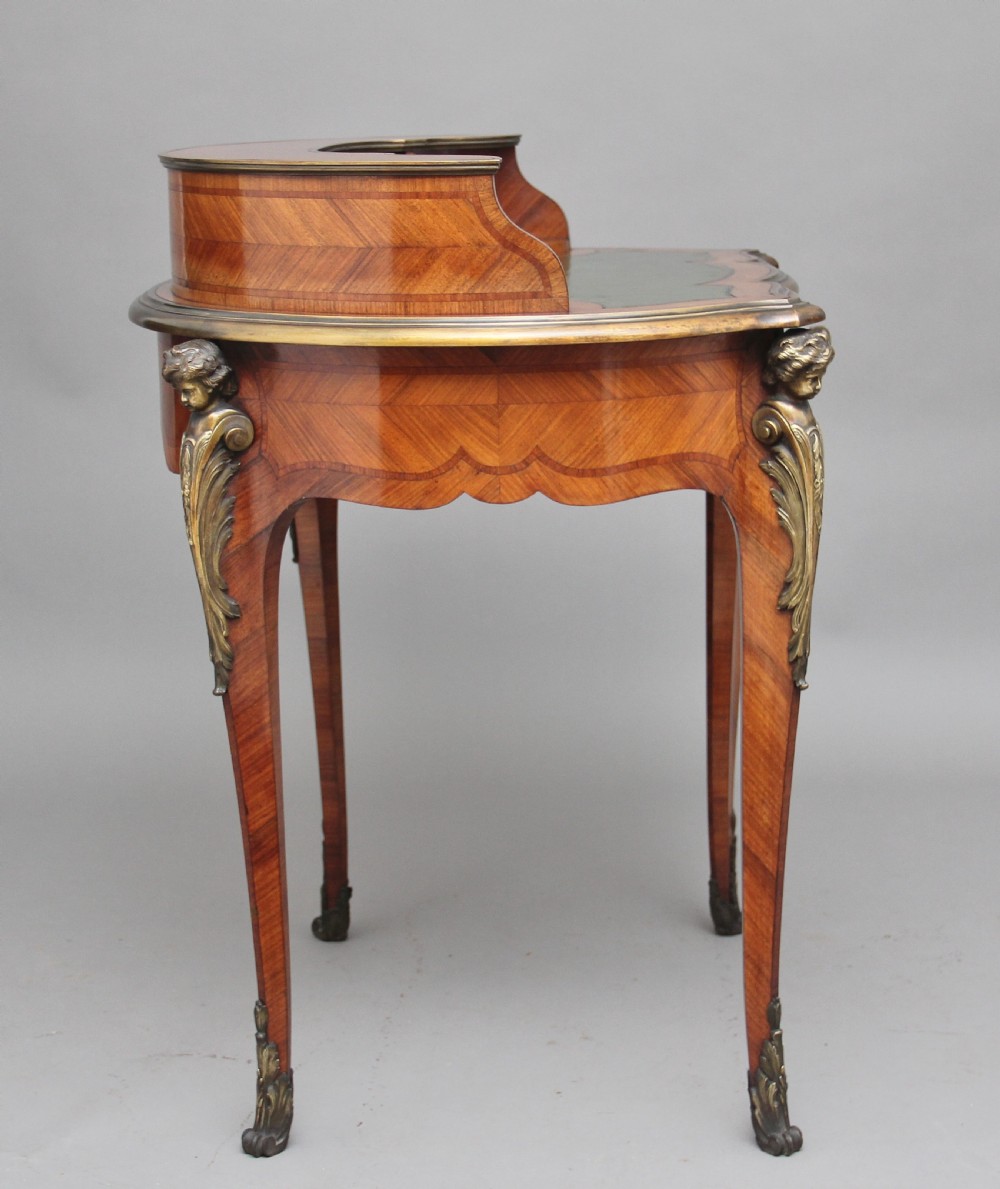 A 19th-century French kingwood writing table featuring ornate gilt-bronze mounts, cabriole legs, a green leather inset top, and a raised shelving superstructure. View VII