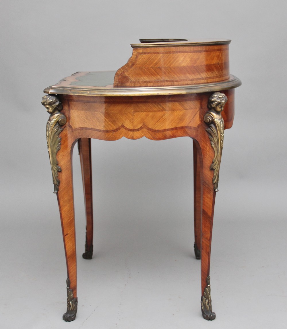 A 19th-century French kingwood writing table featuring ornate gilt-bronze mounts, cabriole legs, a green leather inset top, and a raised shelving superstructure. View IX