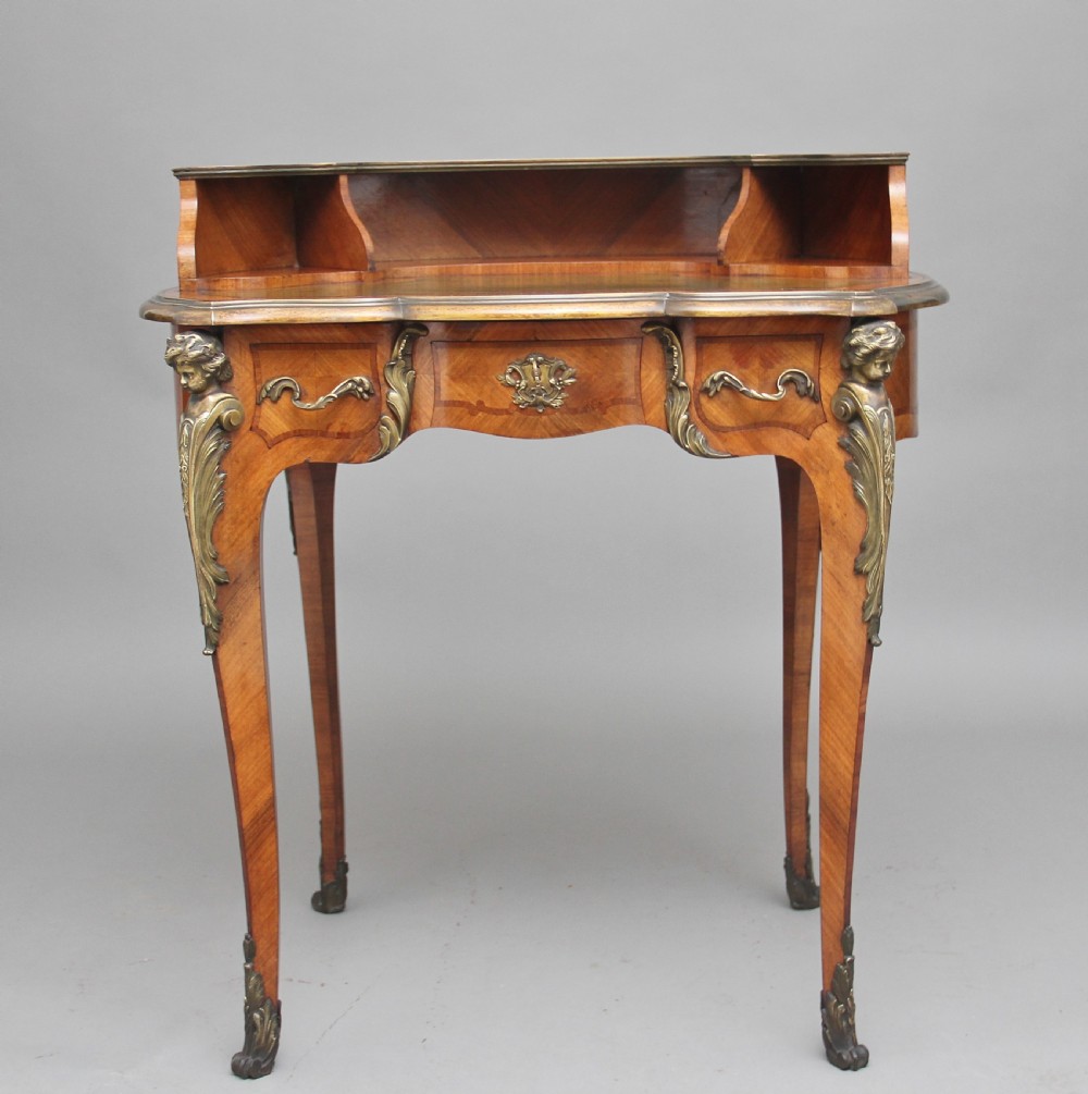A 19th-century French kingwood writing table featuring ornate gilt-bronze mounts, cabriole legs, a green leather inset top, and a raised shelving superstructure. View X