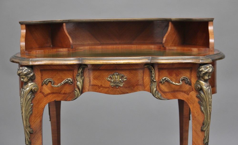 A 19th-century French kingwood writing table featuring ornate gilt-bronze mounts, cabriole legs, a green leather inset top, and a raised shelving superstructure. View XI