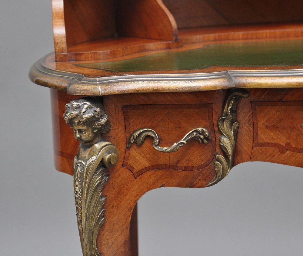 A 19th-century French kingwood writing table featuring ornate gilt-bronze mounts, cabriole legs, a green leather inset top, and a raised shelving superstructure. View XIV