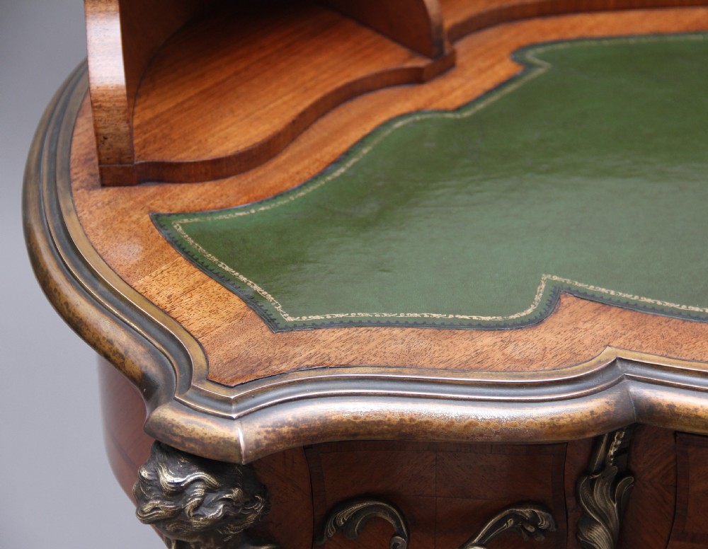 A 19th-century French kingwood writing table featuring ornate gilt-bronze mounts, cabriole legs, a green leather inset top, and a raised shelving superstructure. View XV
