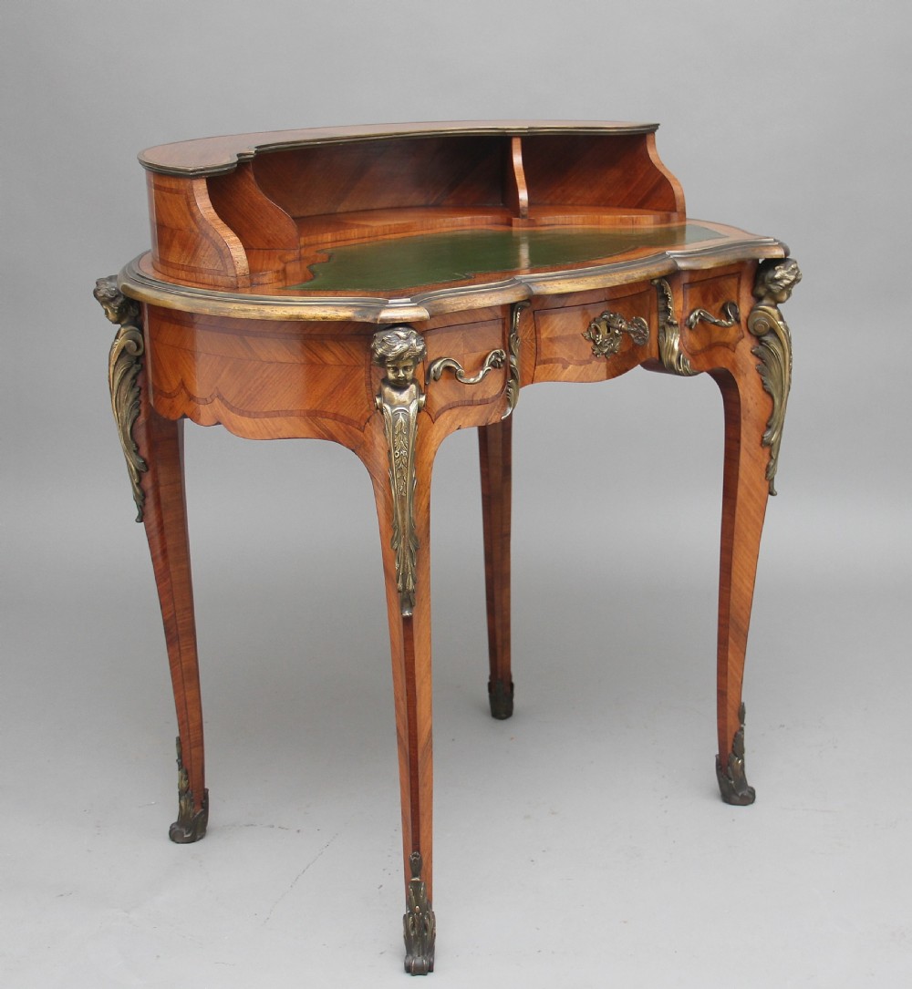 A 19th-century French kingwood writing table featuring ornate gilt-bronze mounts, cabriole legs, a green leather inset top, and a raised shelving superstructure. View XVIII