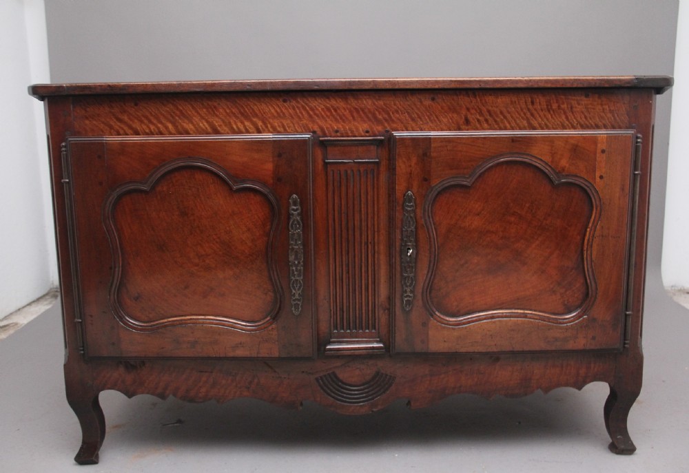 An early nineteenth-century French cherrywood dresser base featuring two cupboard doors with shaped panels, central fluting, decorative brass escutcheons, and short cabriole legs.