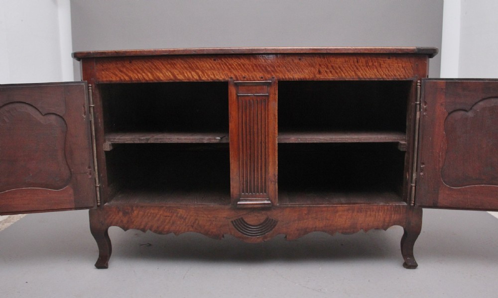 An early nineteenth-century French cherrywood dresser base featuring two cupboard doors with shaped panels, central fluting, decorative brass escutcheons, and short cabriole legs. View II